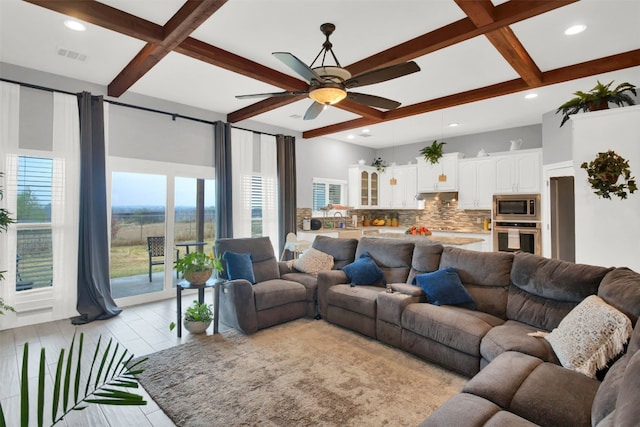 living area featuring ceiling fan, light wood-style flooring, coffered ceiling, visible vents, and beam ceiling