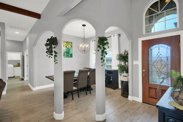 foyer entrance featuring light wood finished floors, visible vents, beam ceiling, washer and dryer, and a notable chandelier