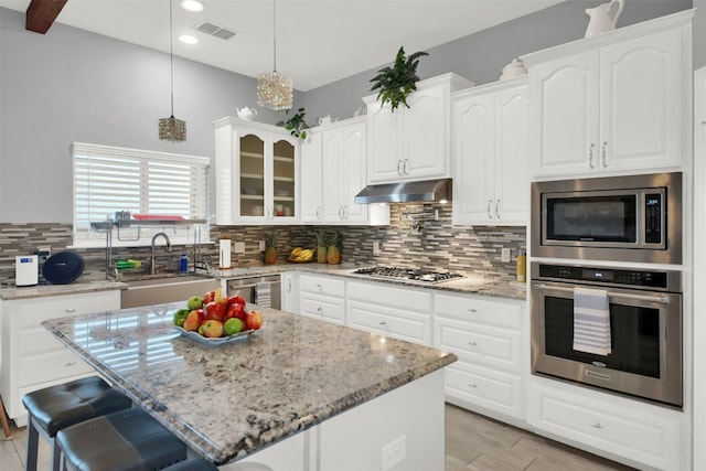 kitchen with light stone countertops, tasteful backsplash, stainless steel appliances, sink, and a center island