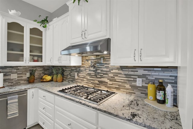 kitchen with glass insert cabinets, light stone counters, stainless steel appliances, under cabinet range hood, and white cabinetry