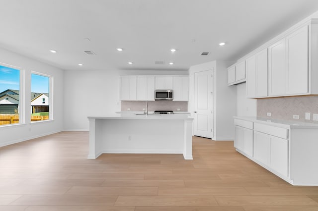 kitchen with stainless steel microwave, light wood-style flooring, and visible vents