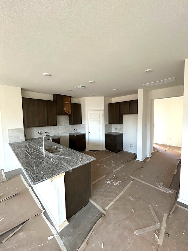 kitchen featuring dark brown cabinetry, light stone countertops, sink, kitchen peninsula, and a textured ceiling