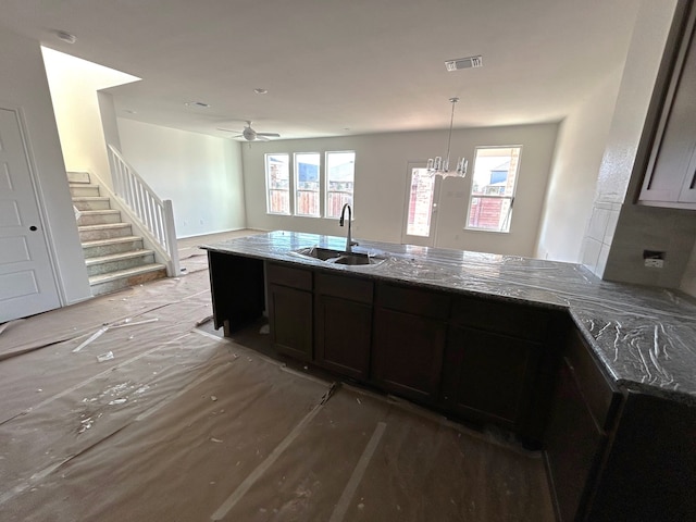 kitchen with dark brown cabinets, a healthy amount of sunlight, dark stone countertops, and sink