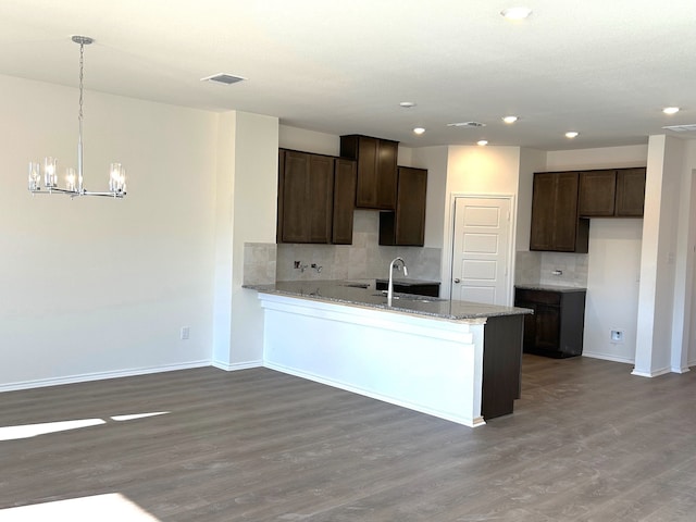 kitchen featuring decorative light fixtures, dark brown cabinetry, light stone counters, and hardwood / wood-style floors