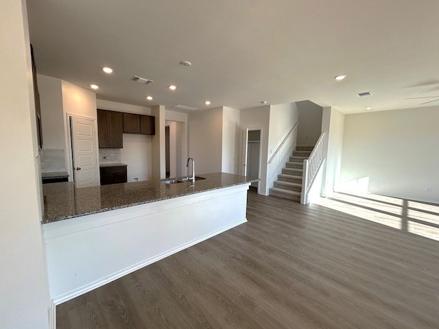 kitchen with dark hardwood / wood-style floors, kitchen peninsula, sink, dark stone counters, and dark brown cabinets