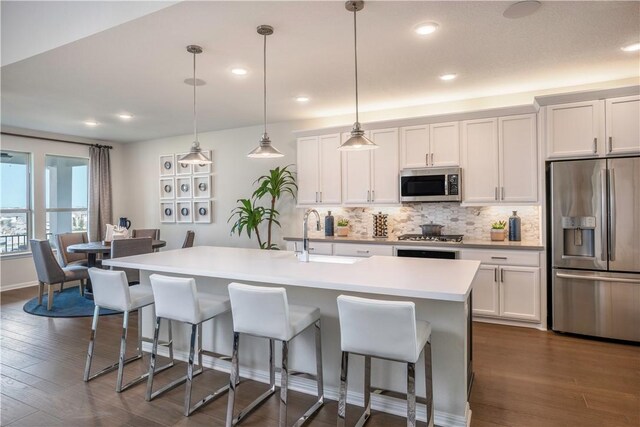 kitchen with dark hardwood / wood-style flooring, stainless steel appliances, sink, pendant lighting, and an island with sink