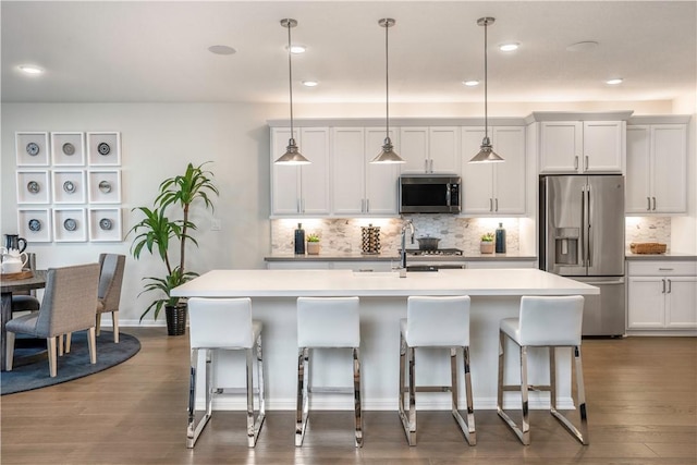 kitchen featuring white cabinetry, an island with sink, decorative light fixtures, and appliances with stainless steel finishes