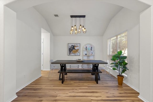 dining area featuring hardwood / wood-style floors, an inviting chandelier, and vaulted ceiling