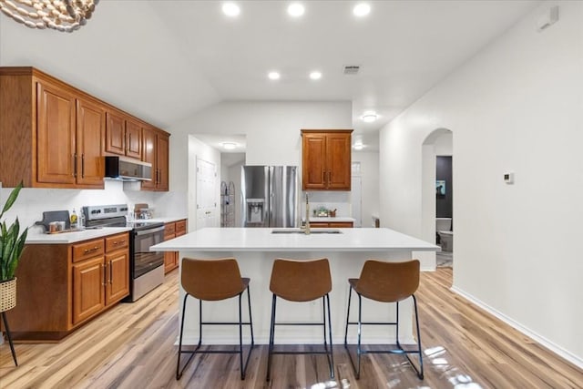 kitchen with a center island with sink, sink, vaulted ceiling, light wood-type flooring, and stainless steel appliances