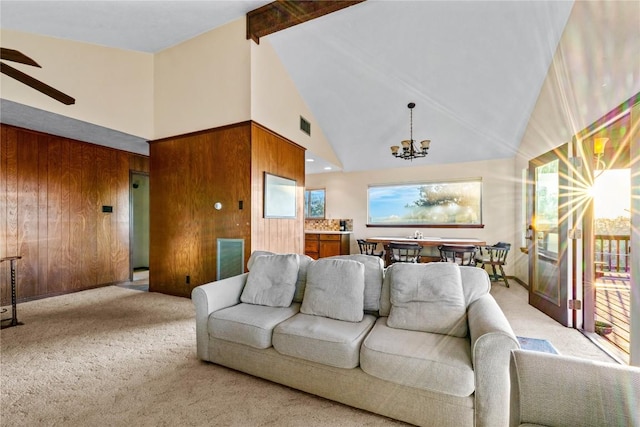 carpeted living room with wooden walls, beamed ceiling, ceiling fan with notable chandelier, and high vaulted ceiling