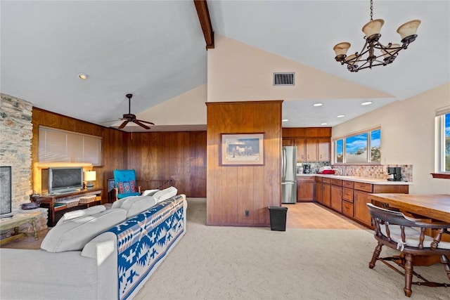 carpeted living room featuring vaulted ceiling with beams, ceiling fan with notable chandelier, sink, and wooden walls