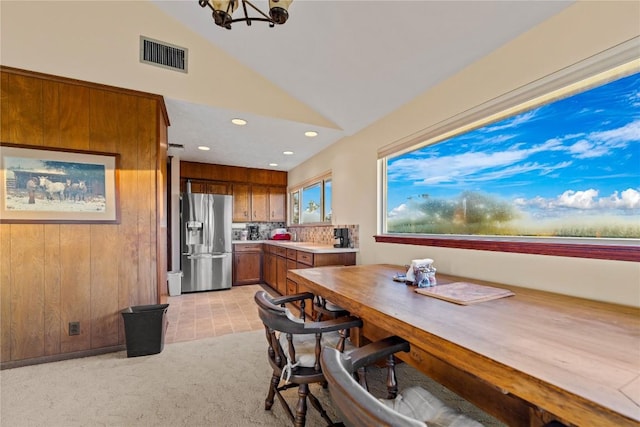 dining area with wood walls, light colored carpet, vaulted ceiling, and an inviting chandelier