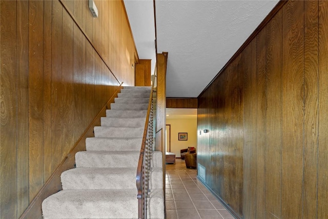 staircase with tile patterned floors, wood walls, and a textured ceiling