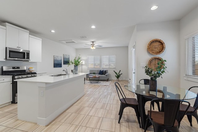 kitchen featuring ceiling fan, a center island with sink, sink, white cabinetry, and stainless steel appliances