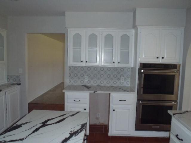 kitchen with decorative backsplash, white cabinetry, stainless steel double oven, and light stone counters