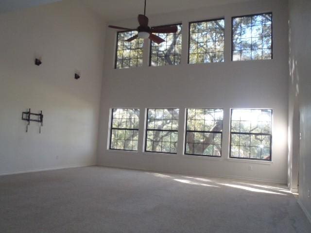 unfurnished living room featuring carpet flooring, a high ceiling, and ceiling fan