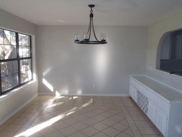 unfurnished dining area featuring plenty of natural light, light tile patterned floors, and an inviting chandelier