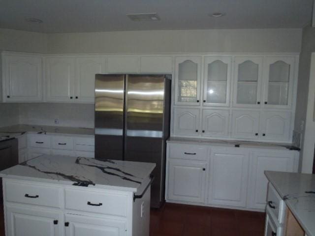 kitchen with white cabinets, a center island, light stone counters, and stainless steel refrigerator with ice dispenser