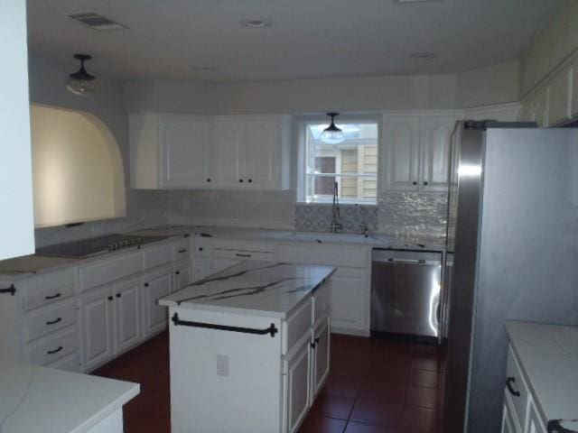 kitchen with white cabinetry, a center island, tasteful backsplash, dark tile patterned floors, and appliances with stainless steel finishes