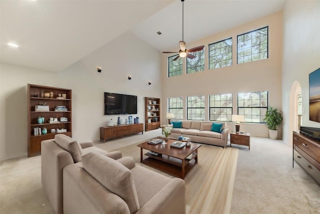 living room featuring a towering ceiling, light colored carpet, and ceiling fan