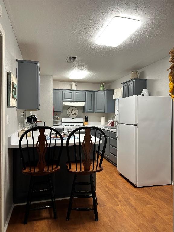 kitchen featuring a textured ceiling, gray cabinets, white appliances, and light wood-type flooring