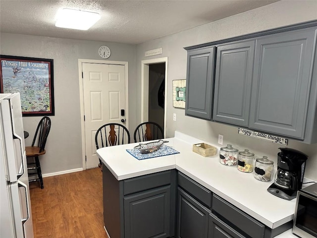 kitchen with gray cabinetry, dark hardwood / wood-style flooring, white refrigerator, kitchen peninsula, and a textured ceiling