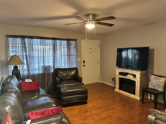 living room with a textured ceiling, ceiling fan, and dark wood-type flooring