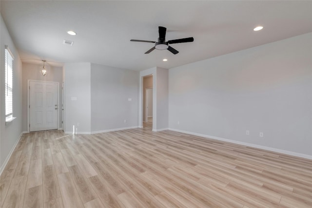 spare room with ceiling fan with notable chandelier and light hardwood / wood-style flooring