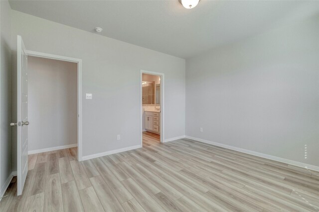 unfurnished bedroom featuring ensuite bathroom and light hardwood / wood-style flooring