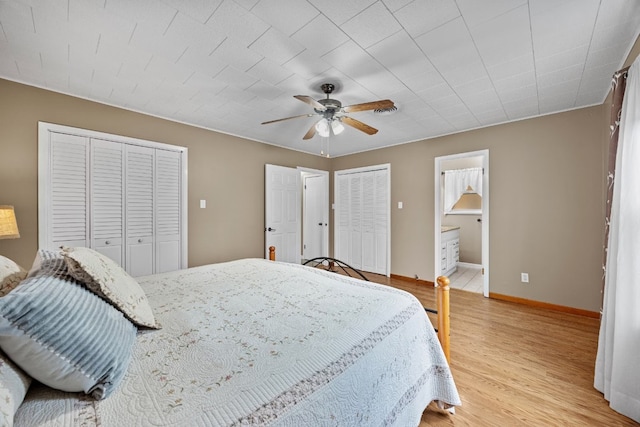 bedroom featuring ensuite bathroom, ceiling fan, light hardwood / wood-style floors, and two closets