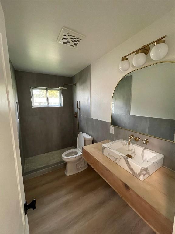 bathroom featuring toilet, wood-type flooring, and tiled shower