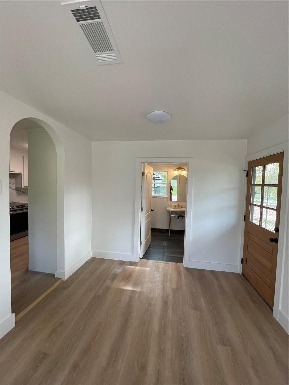 spare room with baseboards, visible vents, arched walkways, and wood finished floors