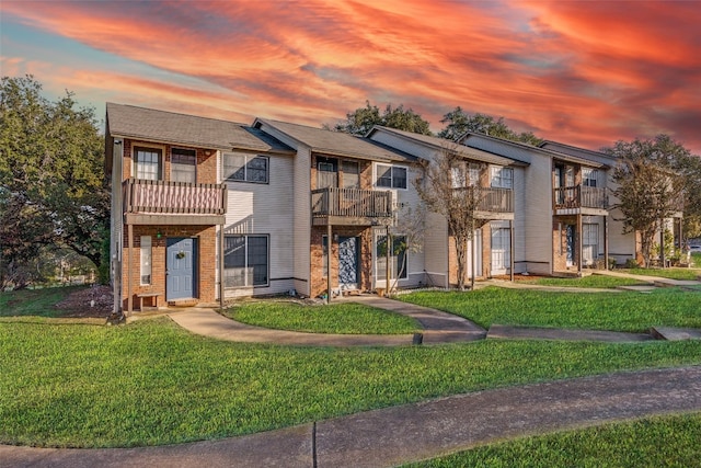 multi unit property with brick siding, a balcony, and a front lawn