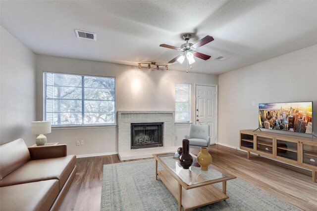 living room featuring ceiling fan, plenty of natural light, a fireplace, and wood-type flooring