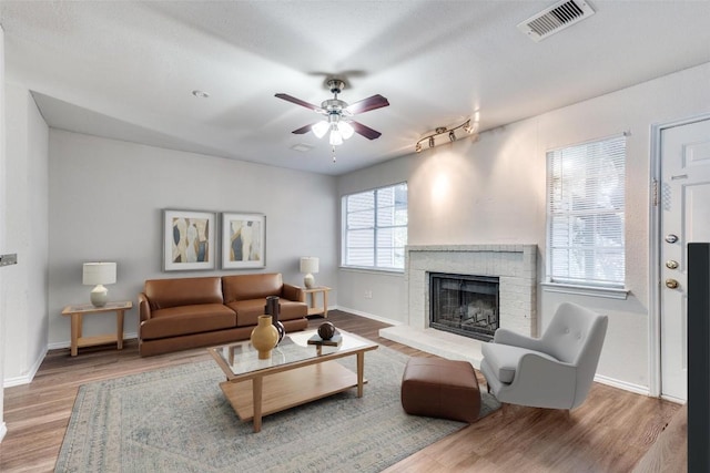 living area with a ceiling fan, a fireplace, visible vents, and wood finished floors