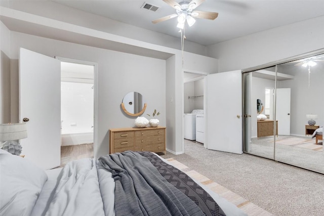 bedroom with visible vents, light colored carpet, ensuite bath, washer and dryer, and a closet