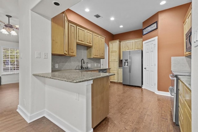 kitchen featuring light stone countertops, sink, kitchen peninsula, wood-type flooring, and appliances with stainless steel finishes