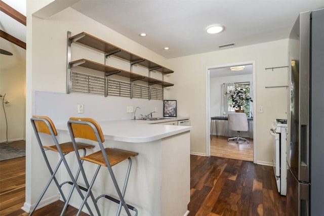 kitchen with kitchen peninsula, stainless steel refrigerator with ice dispenser, white gas range oven, dark hardwood / wood-style floors, and a breakfast bar area