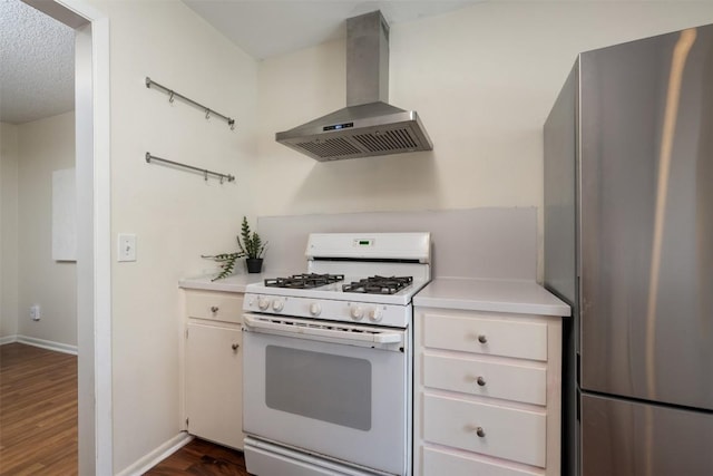 kitchen with stainless steel fridge, dark hardwood / wood-style flooring, gas range gas stove, wall chimney range hood, and white cabinets