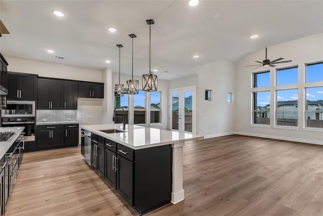 kitchen with appliances with stainless steel finishes, tasteful backsplash, sink, hanging light fixtures, and a kitchen island with sink