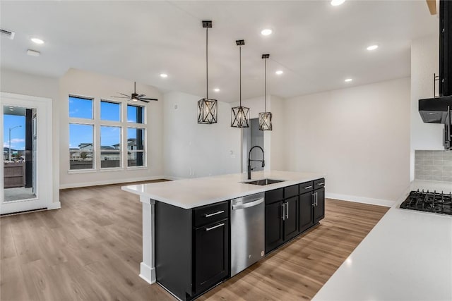 kitchen featuring pendant lighting, sink, light hardwood / wood-style floors, a center island with sink, and stainless steel dishwasher