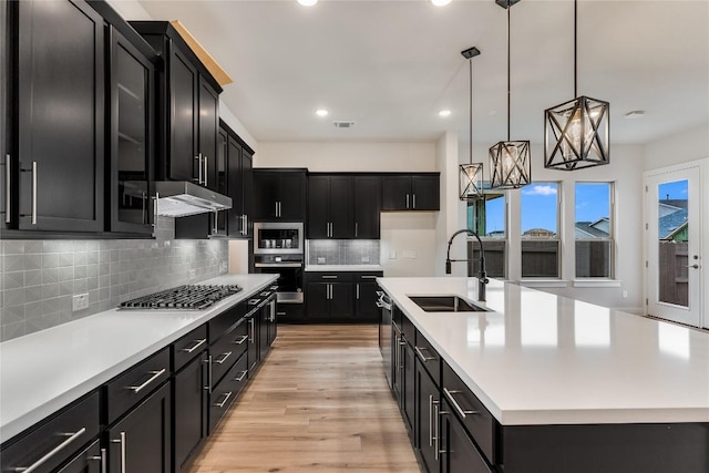 kitchen featuring appliances with stainless steel finishes, decorative light fixtures, sink, decorative backsplash, and a kitchen island with sink