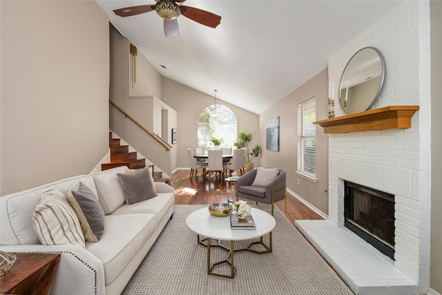 living room featuring ceiling fan, light hardwood / wood-style floors, lofted ceiling, and a brick fireplace