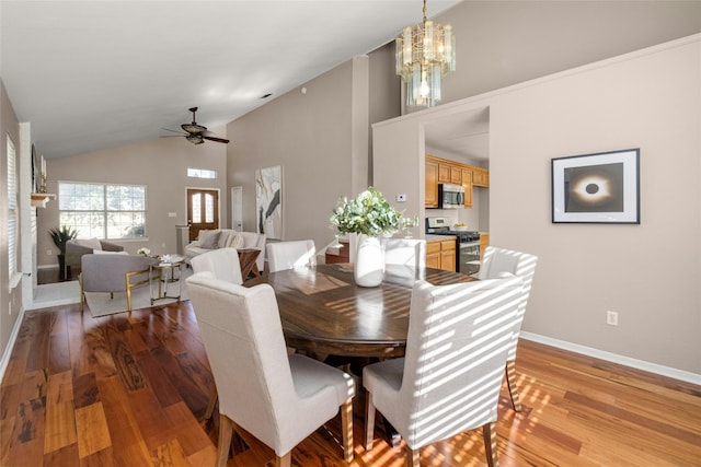 dining space with ceiling fan with notable chandelier, light hardwood / wood-style floors, and vaulted ceiling