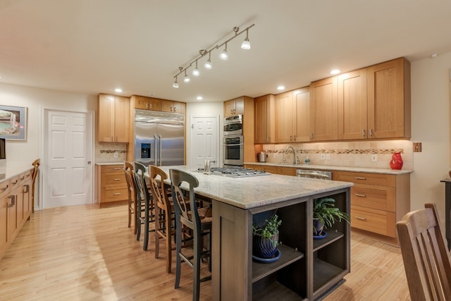 kitchen with decorative backsplash, appliances with stainless steel finishes, light wood-type flooring, sink, and an island with sink