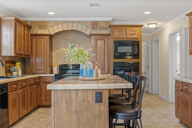 kitchen with a breakfast bar area, a kitchen island, visible vents, black appliances, and crown molding