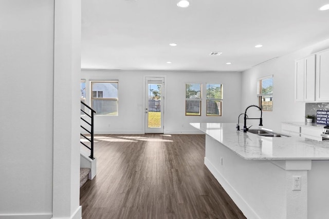 kitchen with white cabinets, light stone counters, sink, and dark wood-type flooring