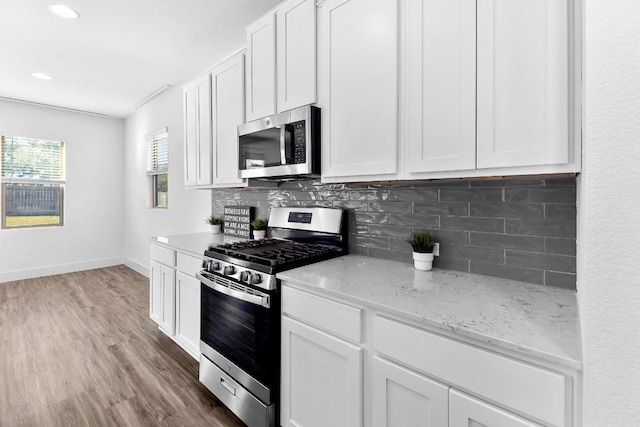 kitchen with decorative backsplash, appliances with stainless steel finishes, white cabinetry, light stone countertops, and light wood-type flooring