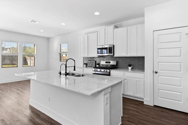 kitchen with stainless steel appliances, a kitchen island with sink, a sink, and white cabinetry