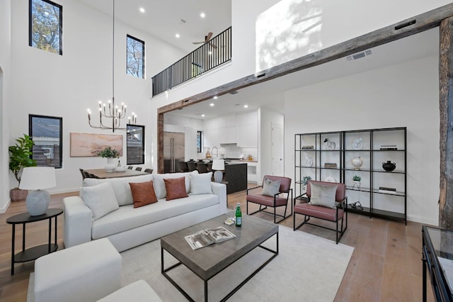 living room with a towering ceiling, a chandelier, and light wood-type flooring